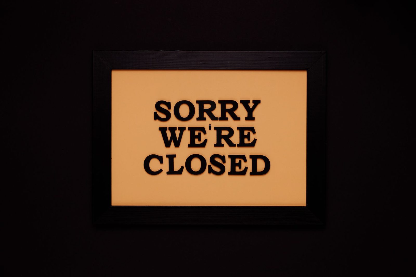 A black-framed "Sorry We're Closed" sign hangs against a dark background.