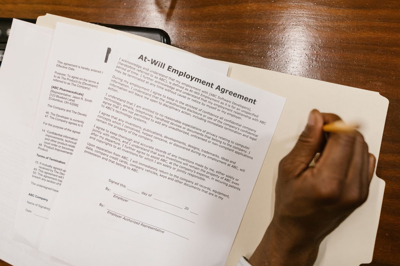 Mano firmando un contrato de trabajo sobre un escritorio de madera.