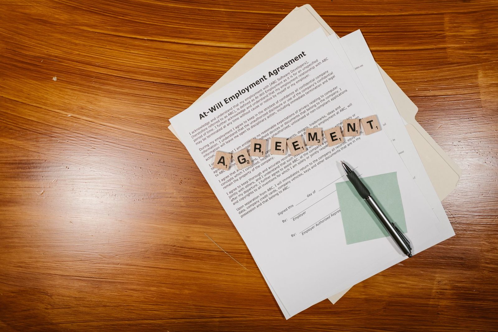 Flat lay of an employment agreement beside Scrabble tiles spelling words on a wooden table.