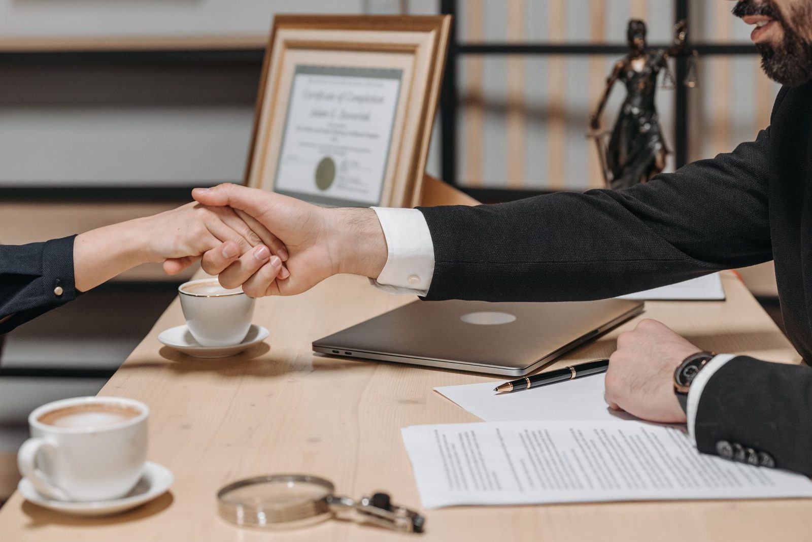 Dos personas se dan la mano sobre un contrato de negocios en una oficina corporativa.