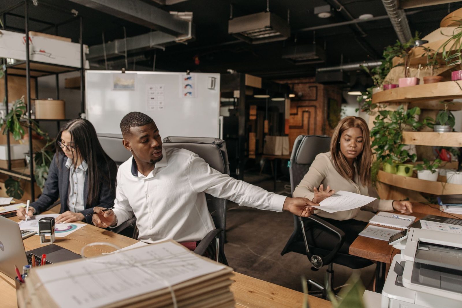 A group of colleagues in a bright, plant-filled office reviewing documents together at a table.