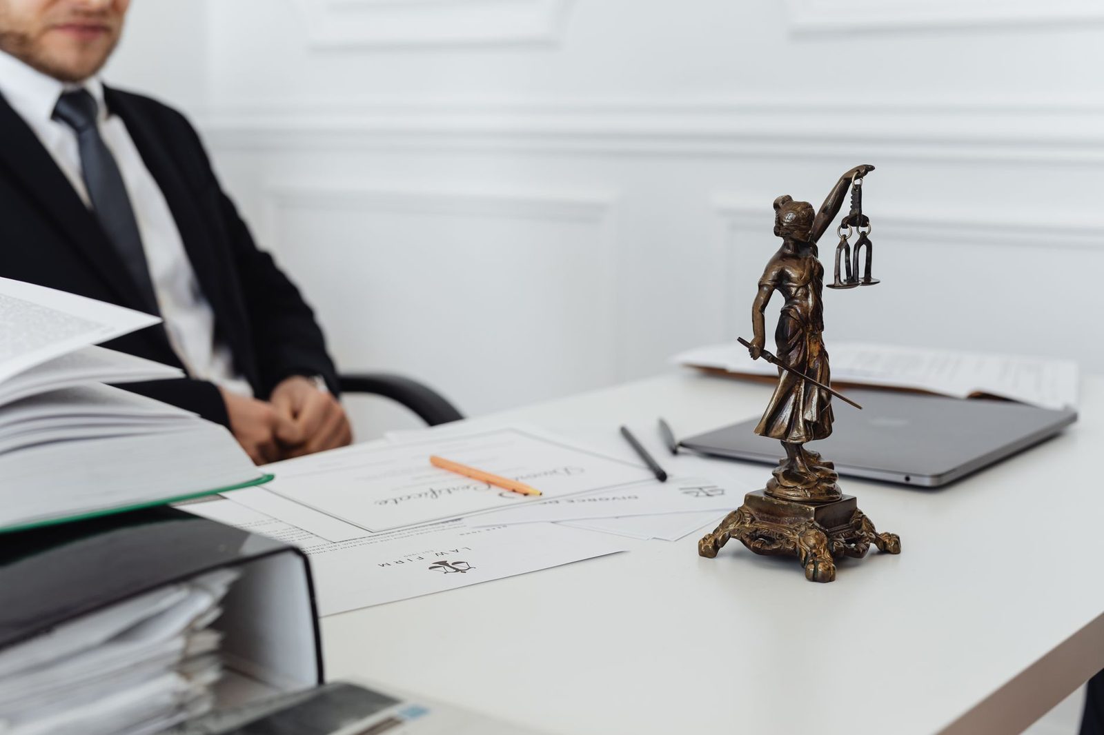 A legal workspace with a Lady Justice statue, stacked documents, and a laptop on a desk.