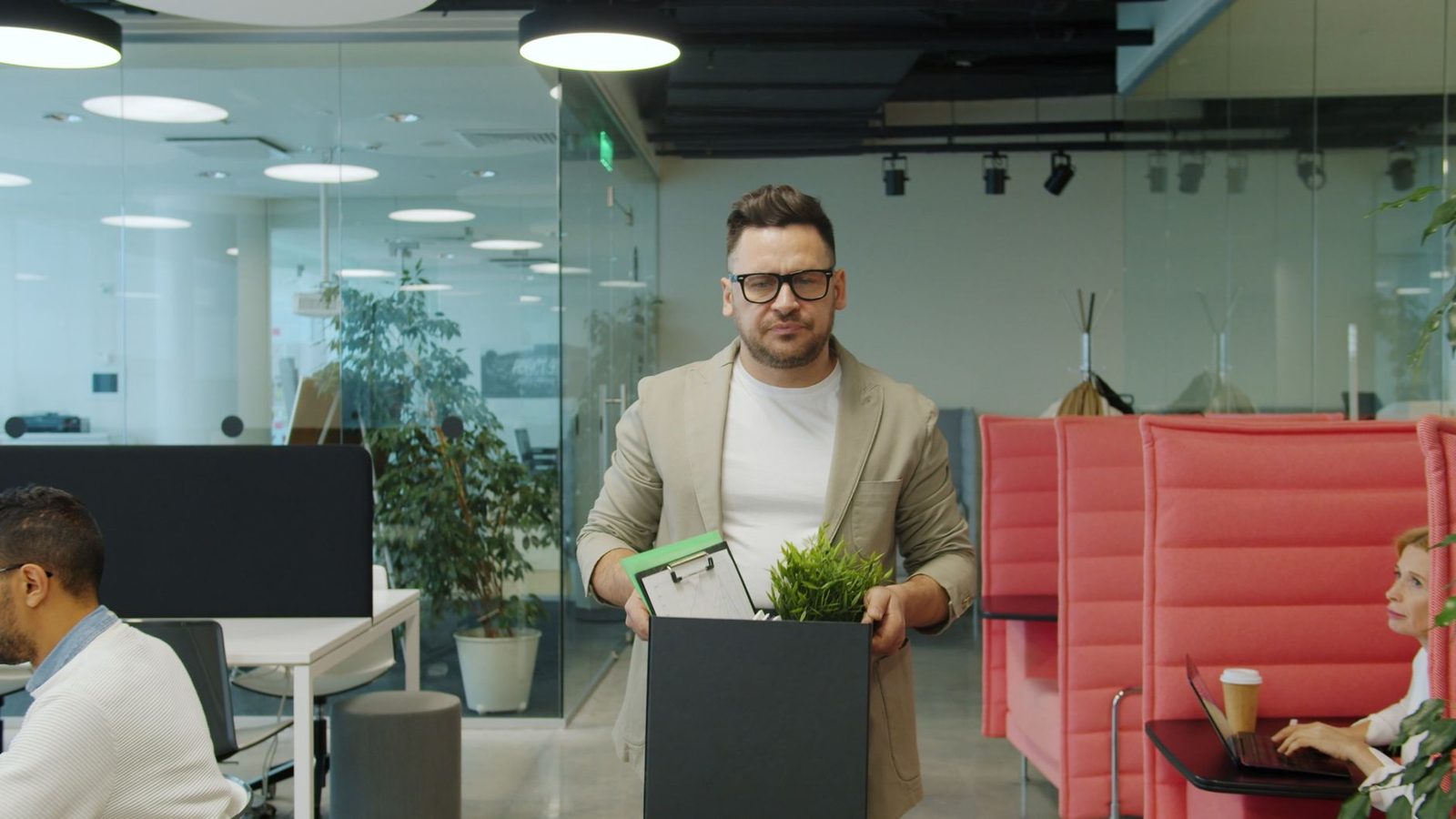 A man carries a cardboard box of belongings out of an office after being let go.