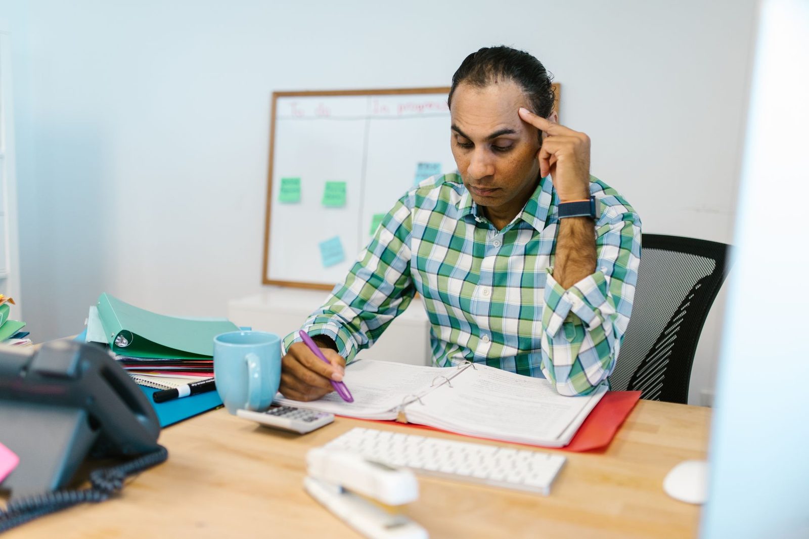 A man at an office desk reviews papers and highlights text with focused determination.