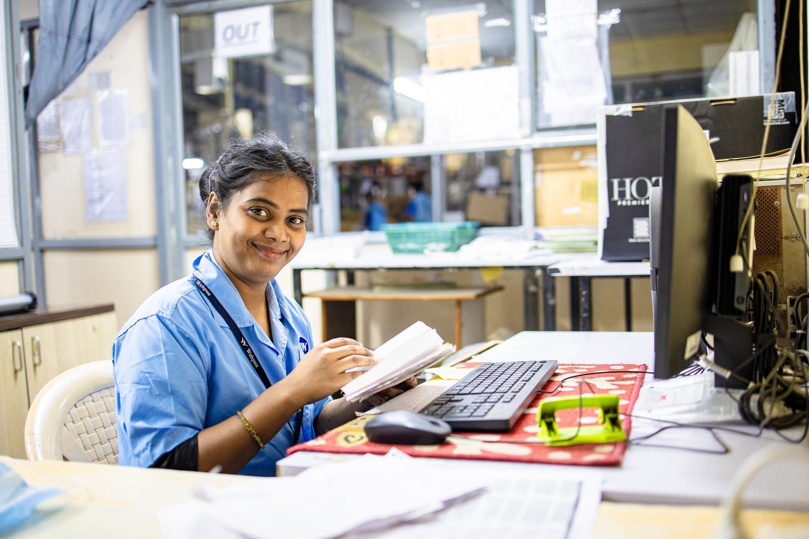 A smiling woman sits at an office desk, reviewing documents.