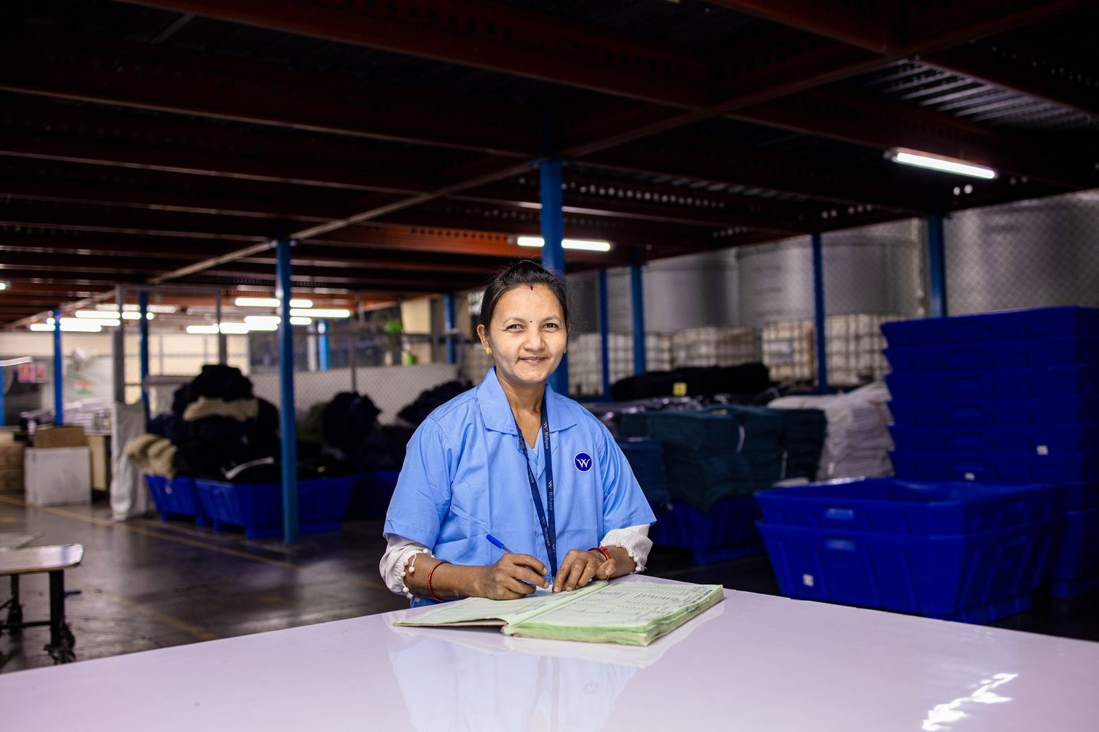 Una mujer con uniforme escribe en una libreta dentro de un almacén textil.