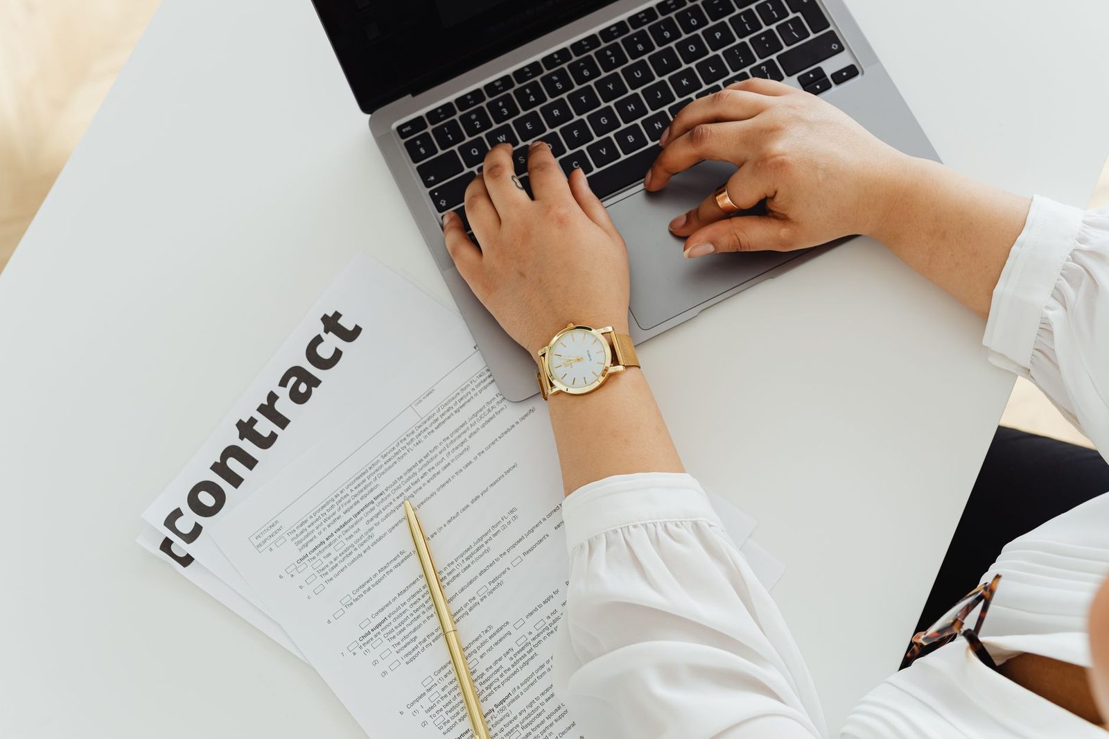 Una mujer trabaja en su laptop junto a un contrato sobre un escritorio, reflejando el trabajo empresarial y legal.