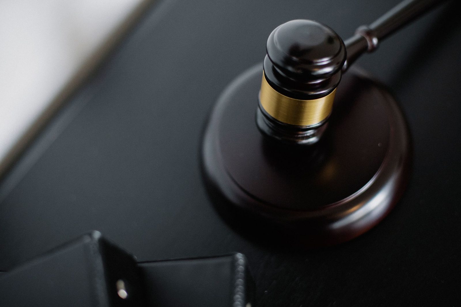 A wooden gavel rests on a round surface beside folders on a table in a courtroom, seen from above.