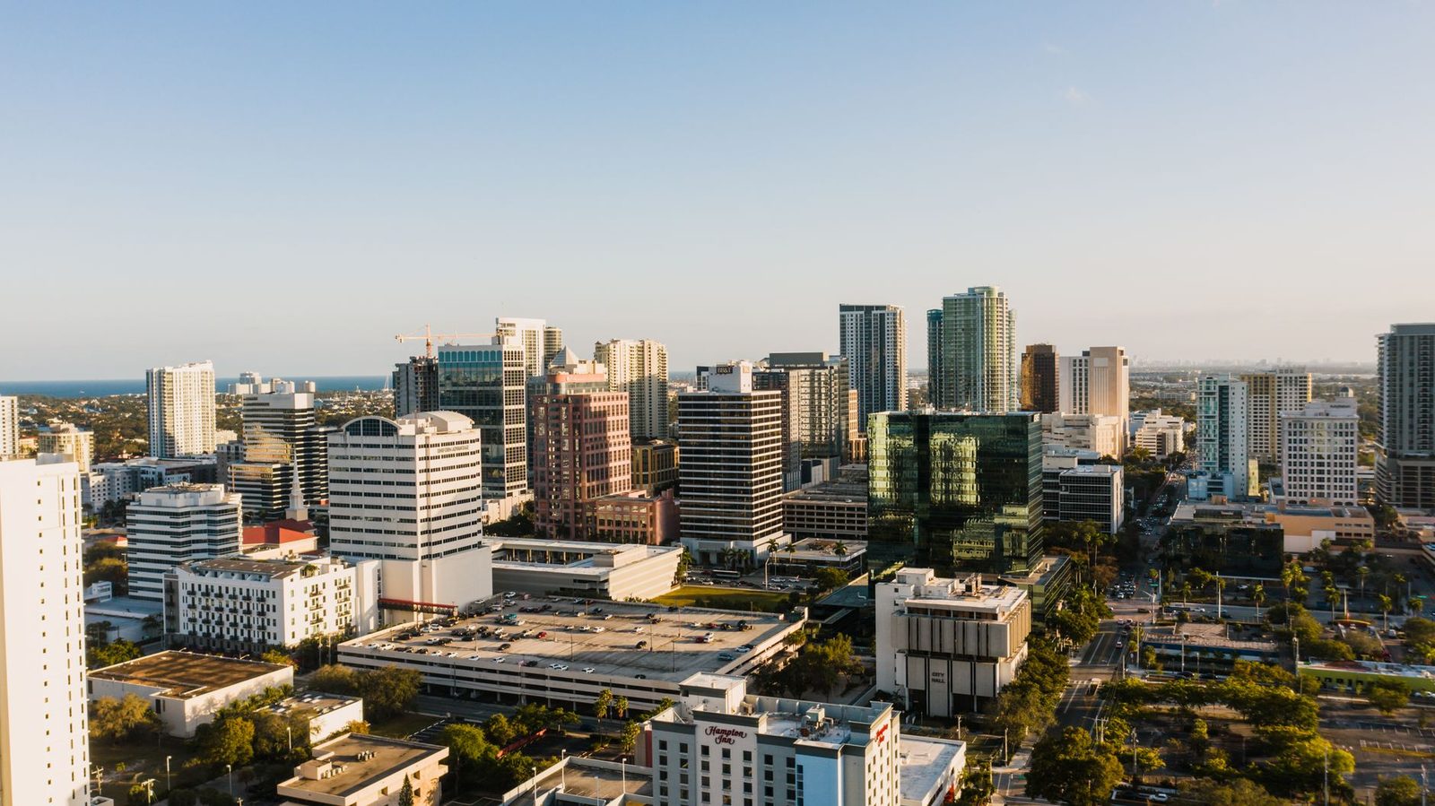 Aerial view of a modern city district with contemporary buildings and green trees under a clear blue sky.