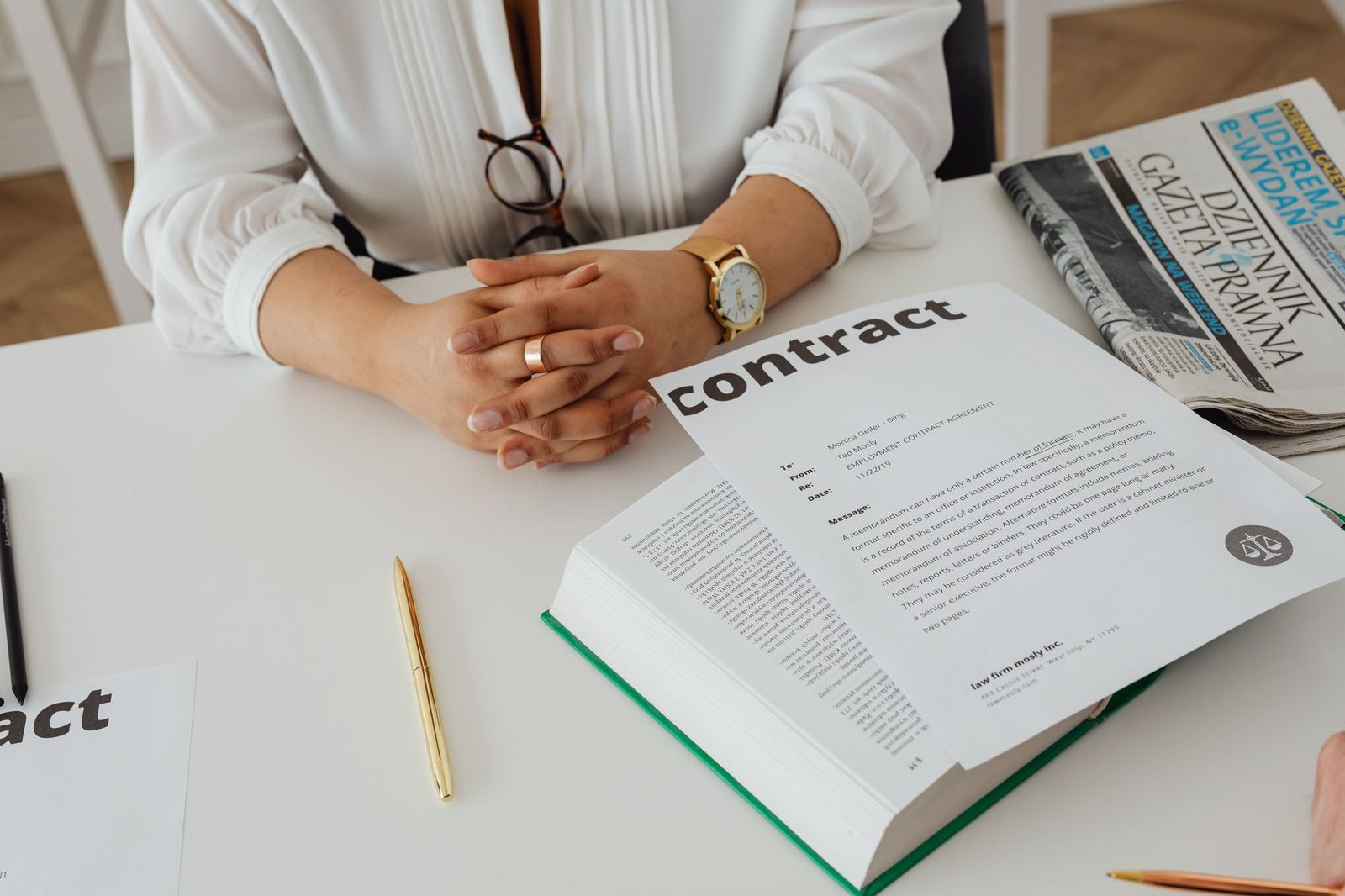 Businesswoman reviewing a contract at a desk beside stacked legal documents and a newspaper.