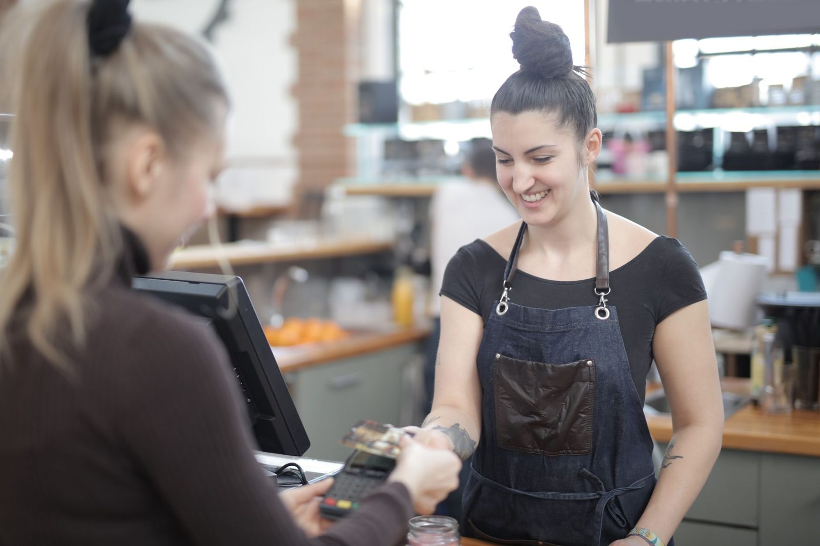 Cajera sonriente ayudando a cliente con pago en mostrador de tienda.