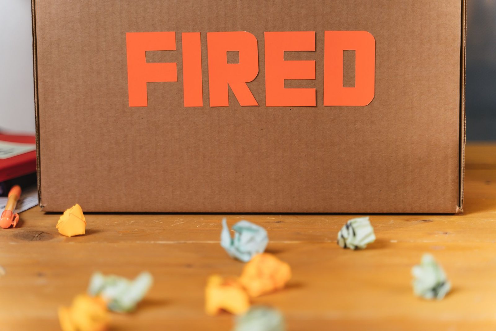Cardboard box labeled "FIRED" on a wooden table beside crumpled papers.