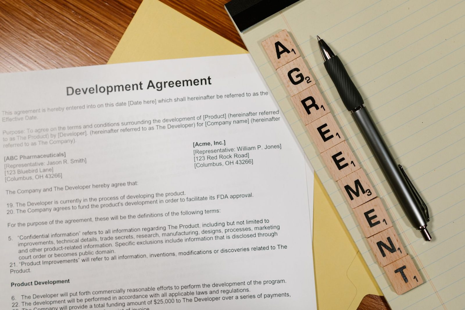 Close-up of a development agreement document beside a pen, with Scrabble tiles spelling "AGREEMENT.