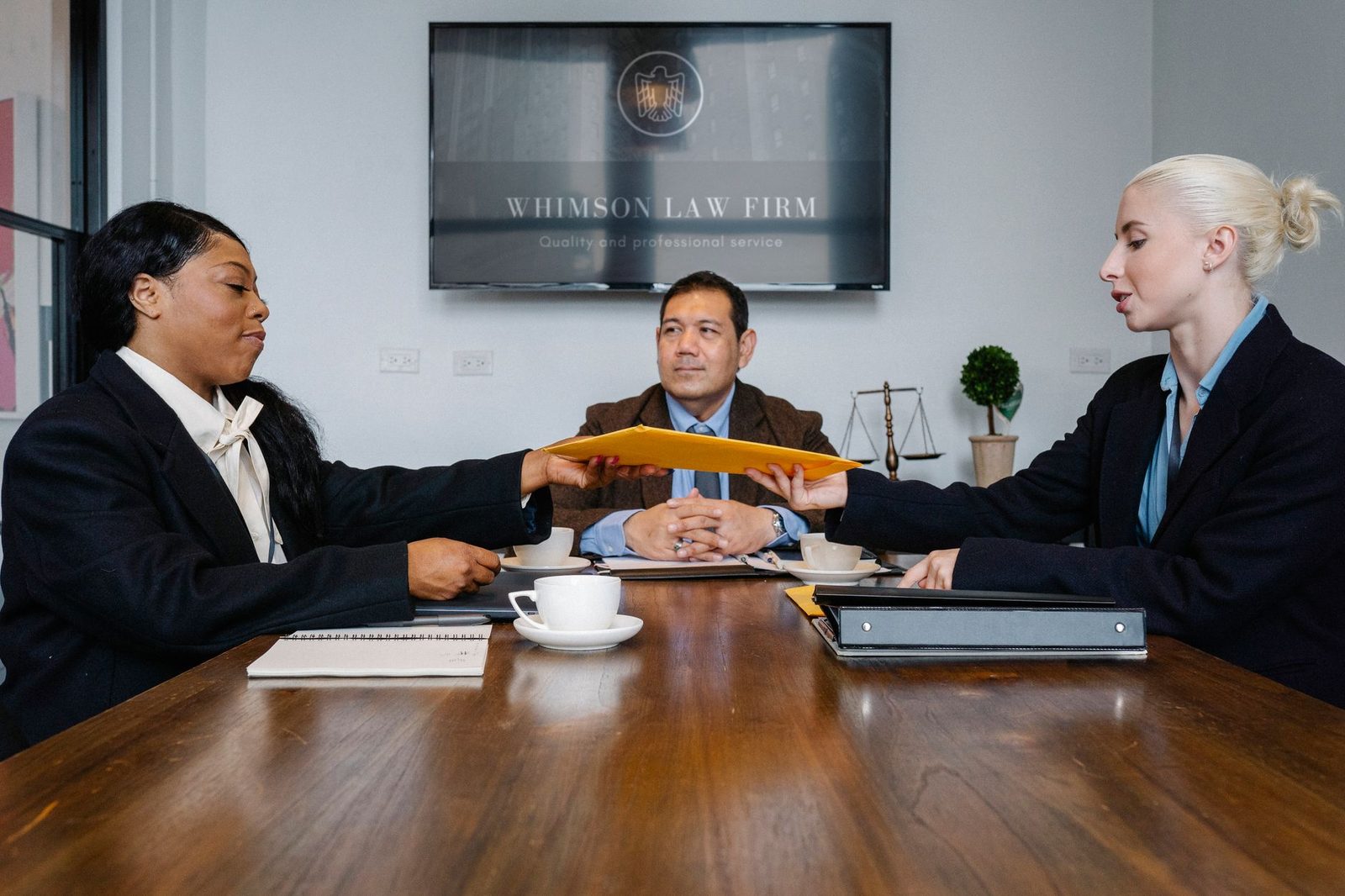 Diverse group of cheerful colleagues discussing a case at a table with a notepad and coffee cup.
