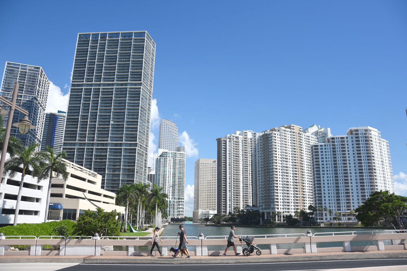 Downtown Miami skyscrapers under a clear blue sky, with pedestrians walking across a bridge.