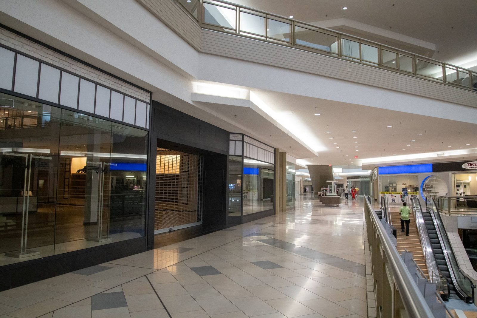 Interior de un centro comercial vacío y moderno, con locales cerrados y una escalera mecánica.
