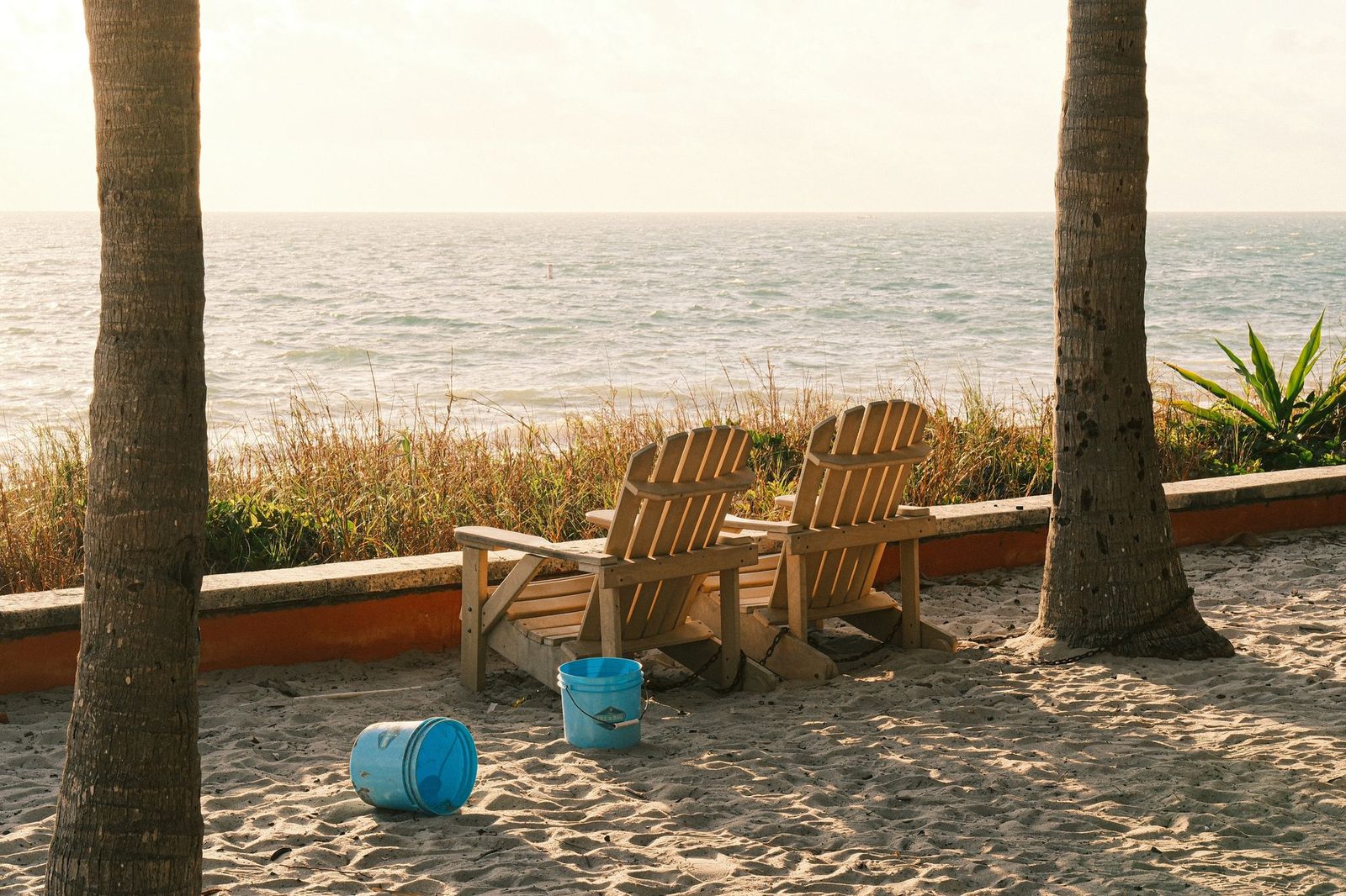 Empty wooden beach chairs face the ocean on a sunny shoreline in Key Biscayne, Florida.