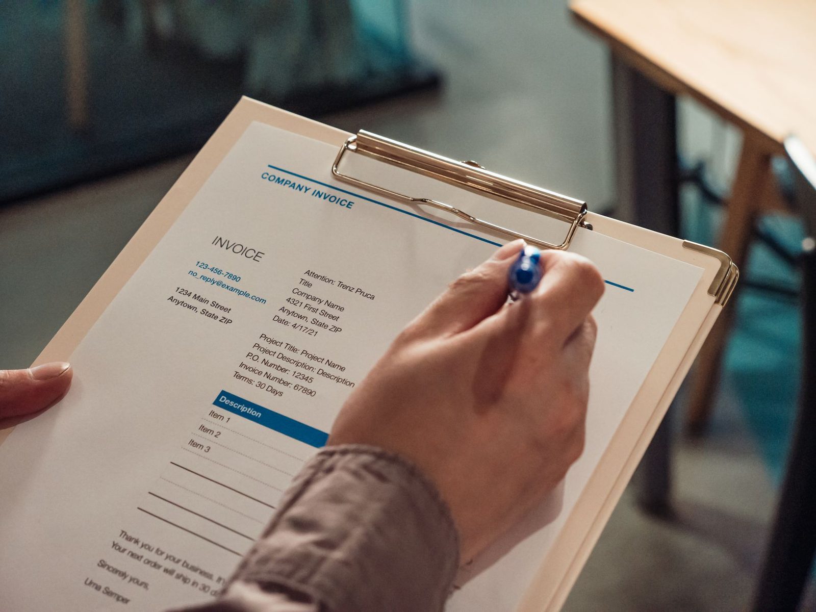 Hand holding a clipboard with an invoice and a pen.