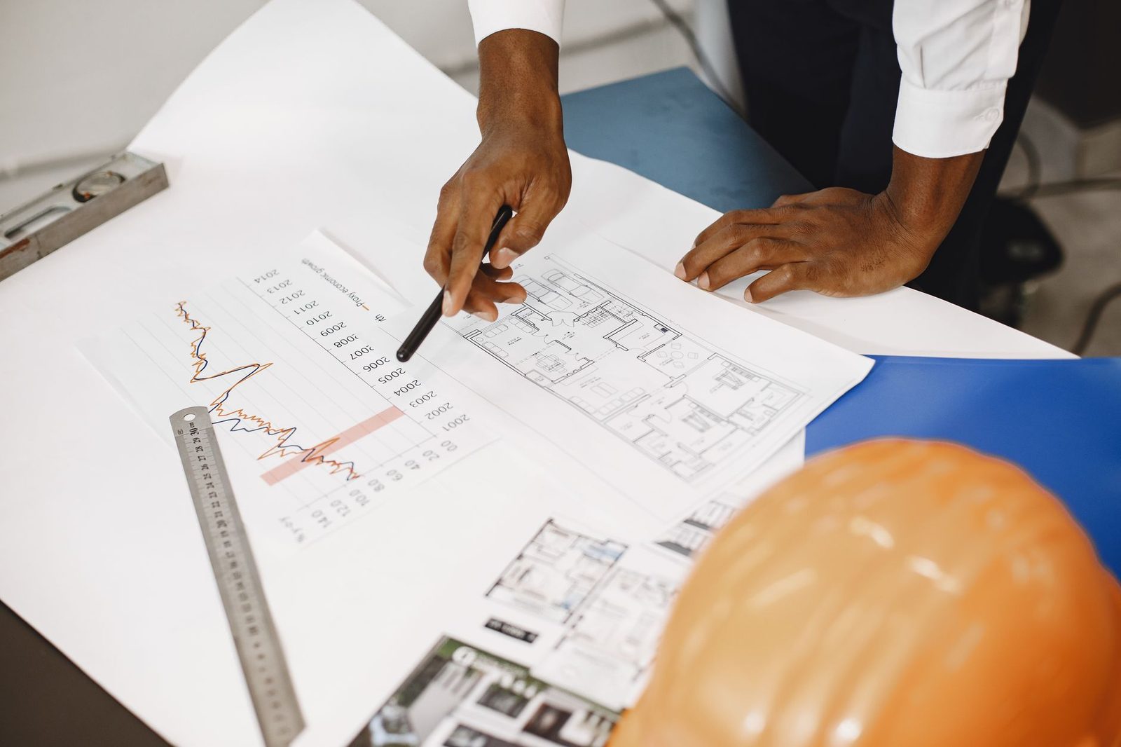Manos sobre planos arquitectónicos junto a gráficos financieros impresos en un escritorio.