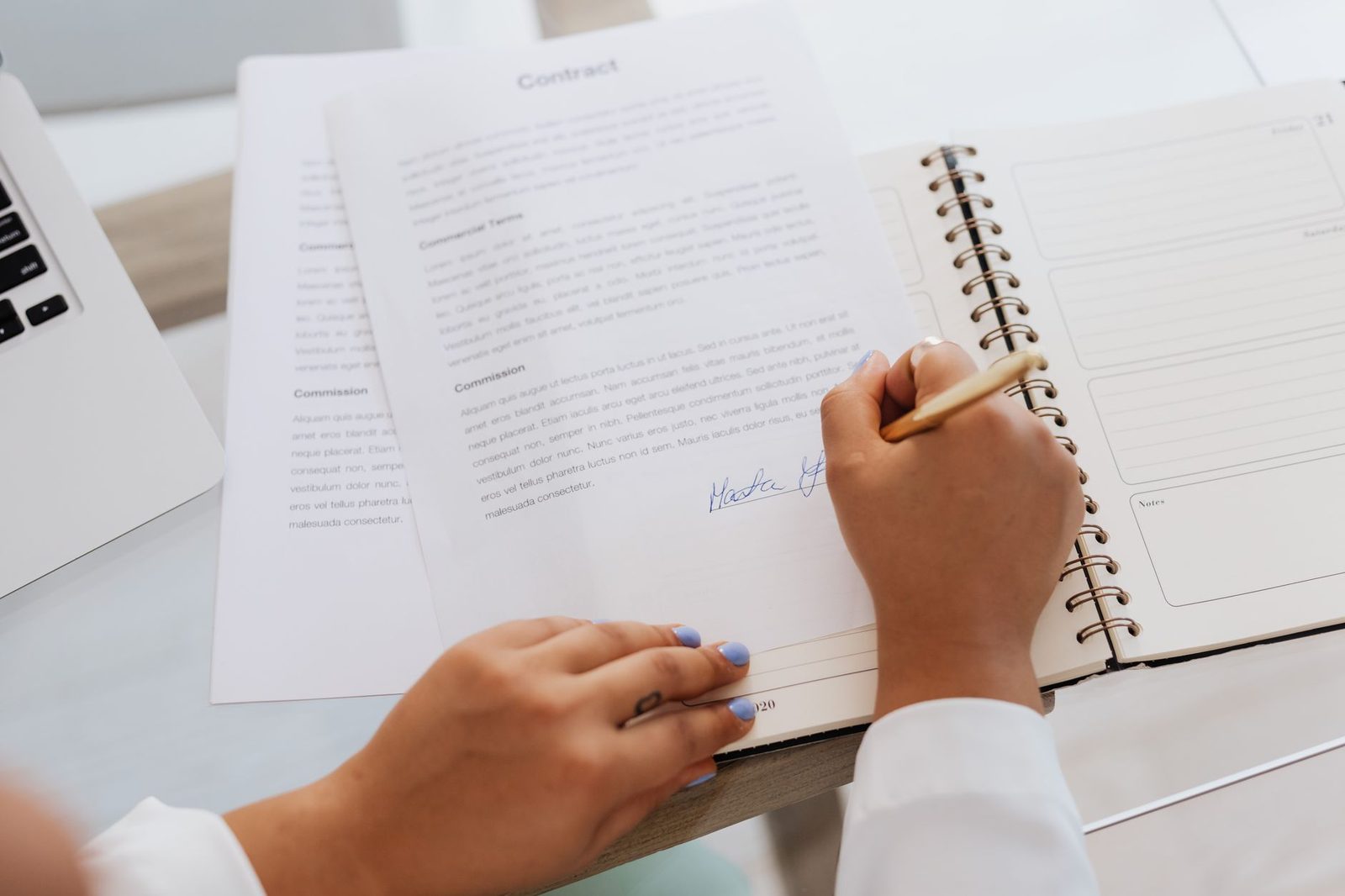 Hands signing a contract on a desk beside pens and office supplies.