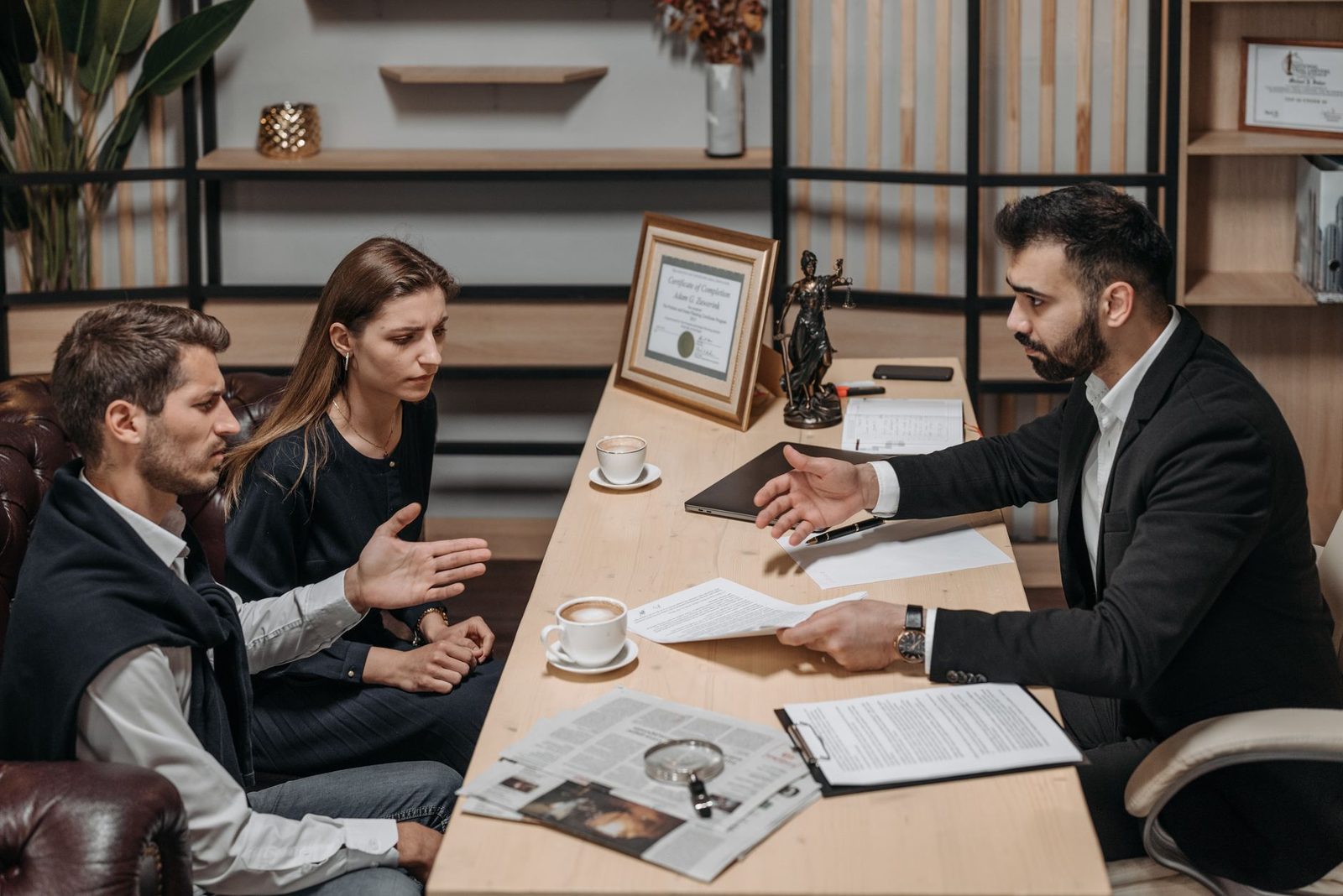 Two attorneys meet with clients at a conference table covered in documents and coffee cups in a Miami-Dade law office.