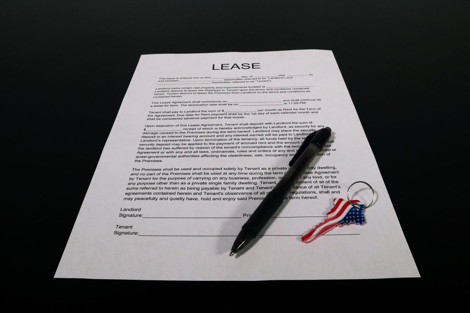 Lease agreement document with a pen and American flag keychain resting on a black table.