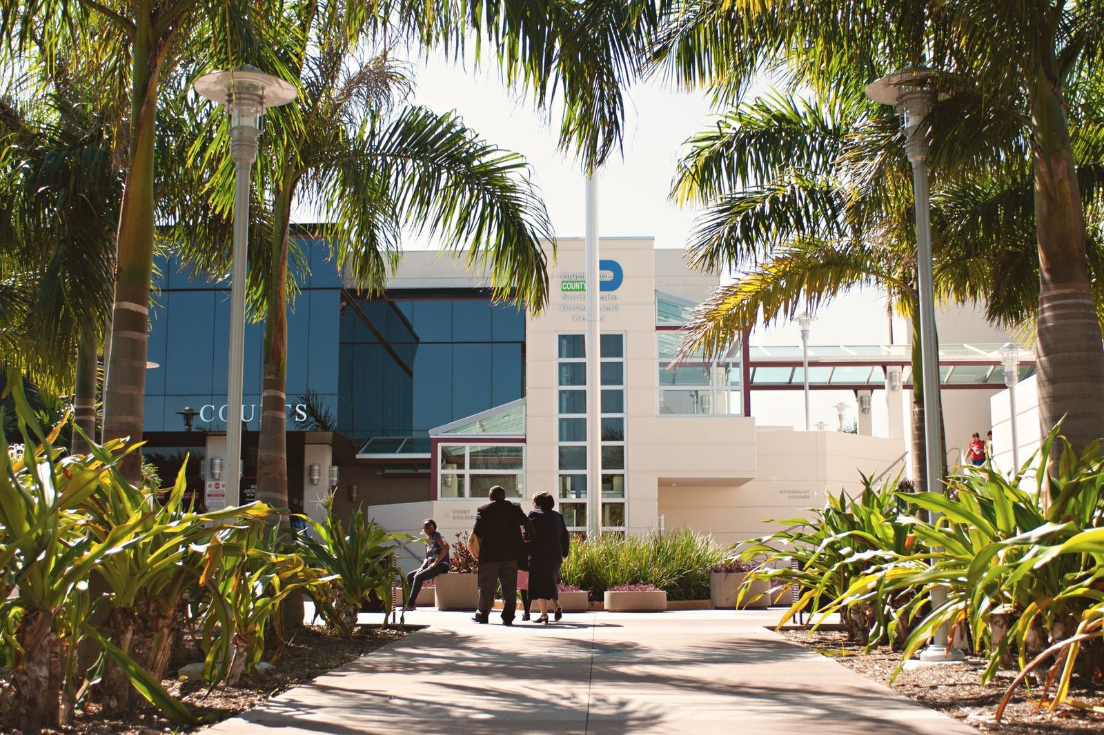 Exterior de un moderno edificio de tribunales en Miami rodeado de altas palmeras, con personas caminando cerca.