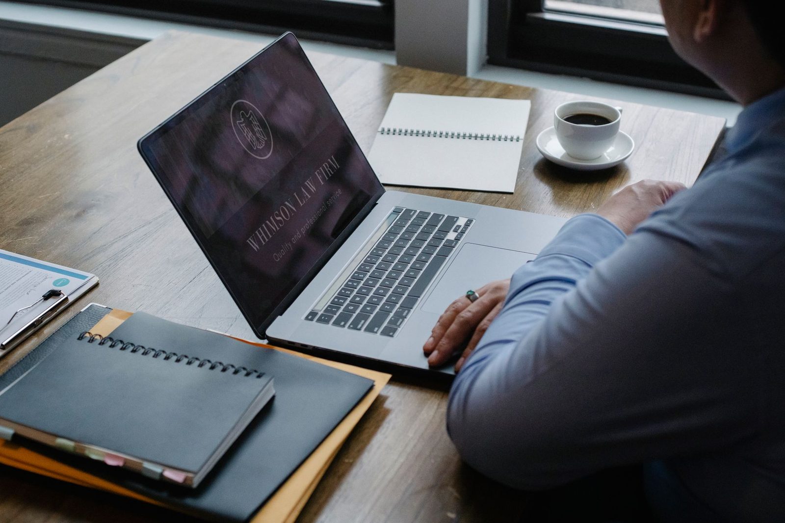 A businessman using a netbook at a table beside documents and a cup of hot coffee, shot from above.