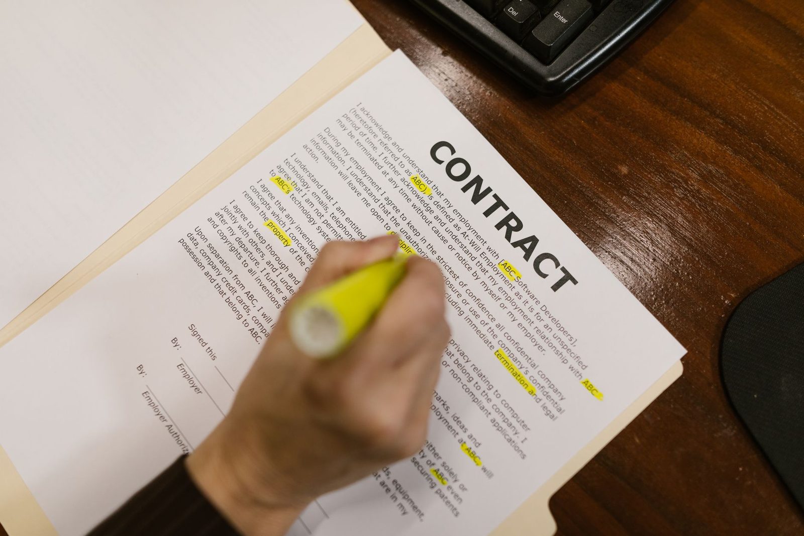 Persona subrayando un pasaje de un contrato sobre un escritorio de madera.