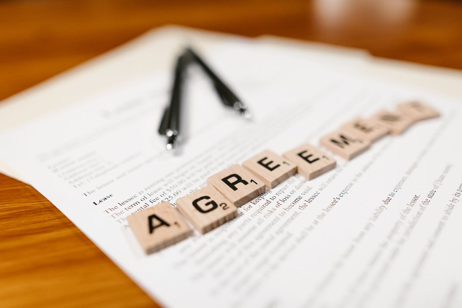 Fichas de Scrabble que deletrean "AGREEMENT" sobre un documento de arrendamiento.