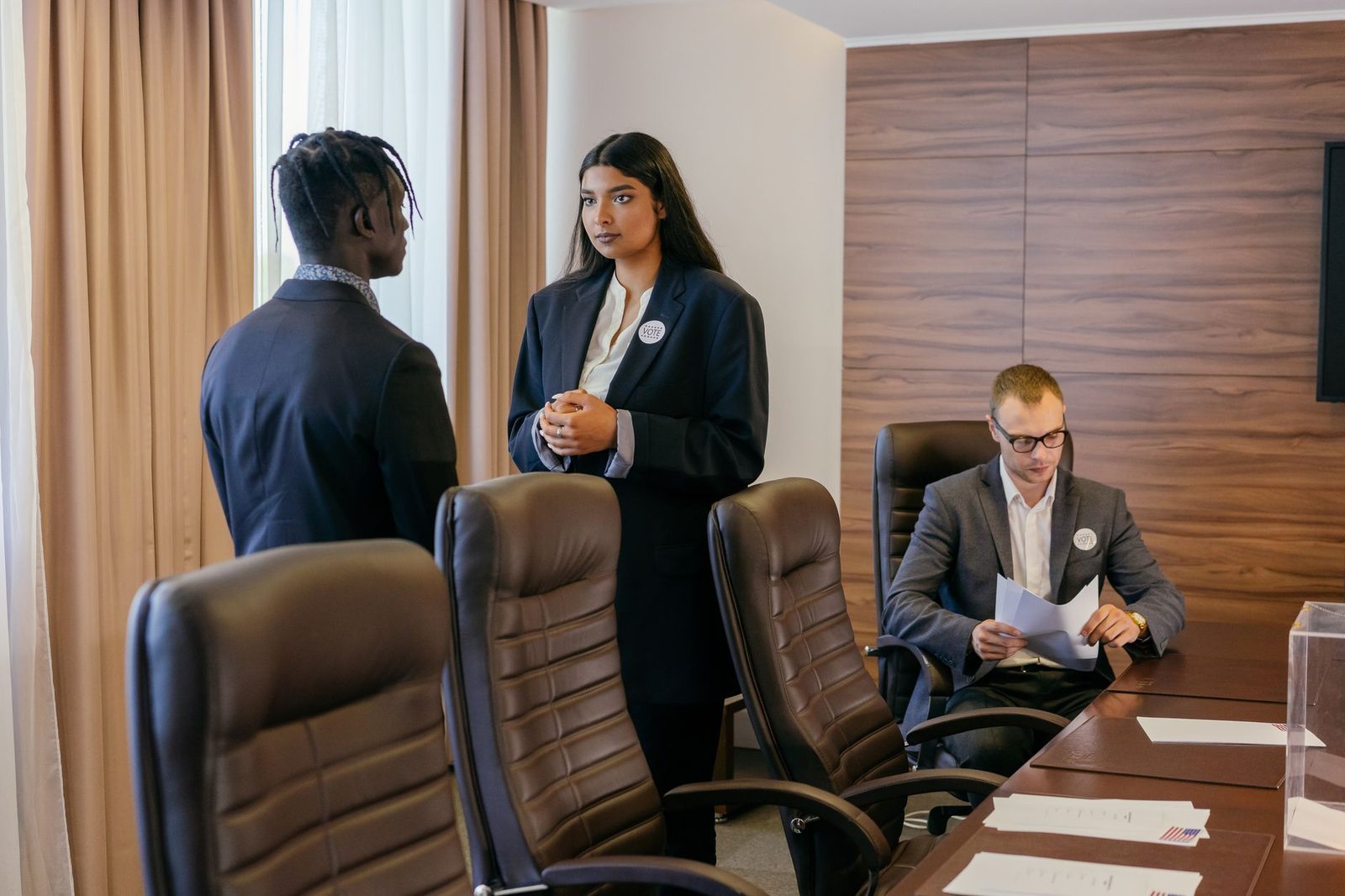 Three professionals gather around a table in a modern conference room, discussing business strategy.