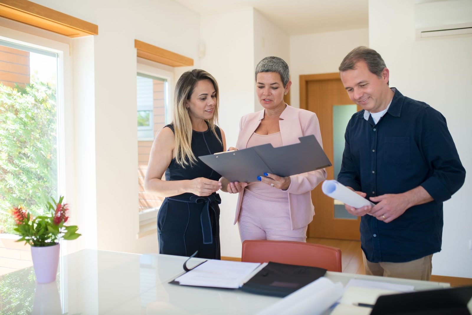 Tres profesionales inmobiliarios revisan documentos juntos en un escritorio de una oficina moderna.