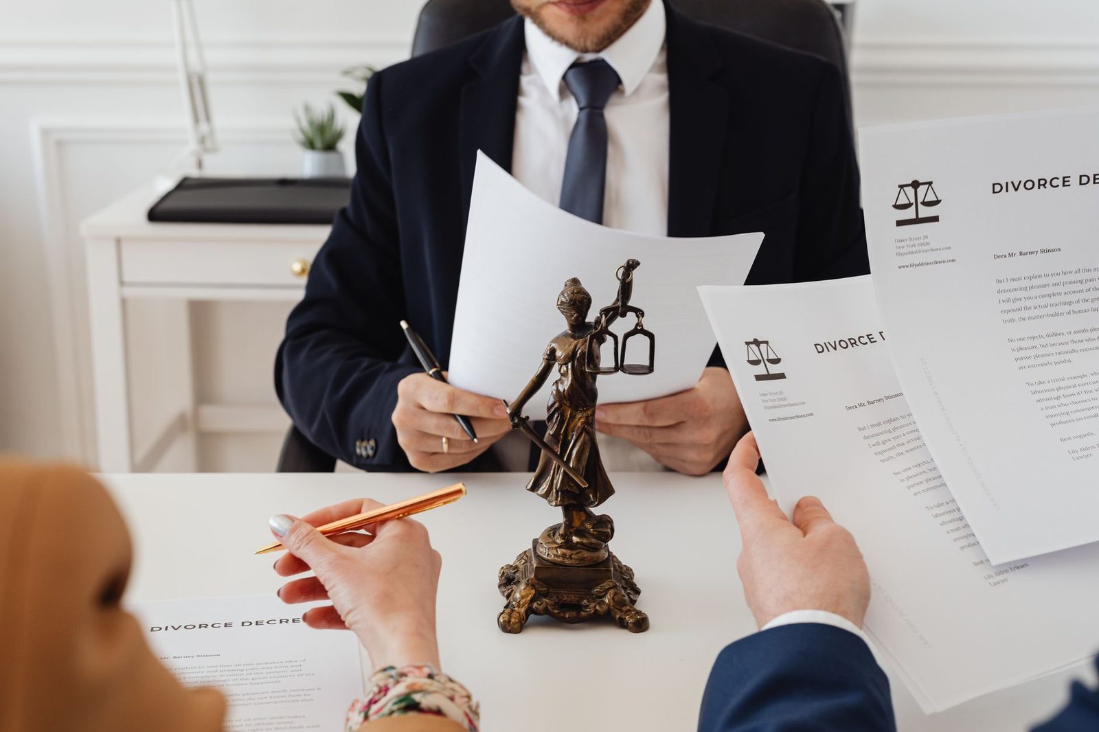 Two attorneys review divorce paperwork at a desk beside a Lady Justice statue in a law office.