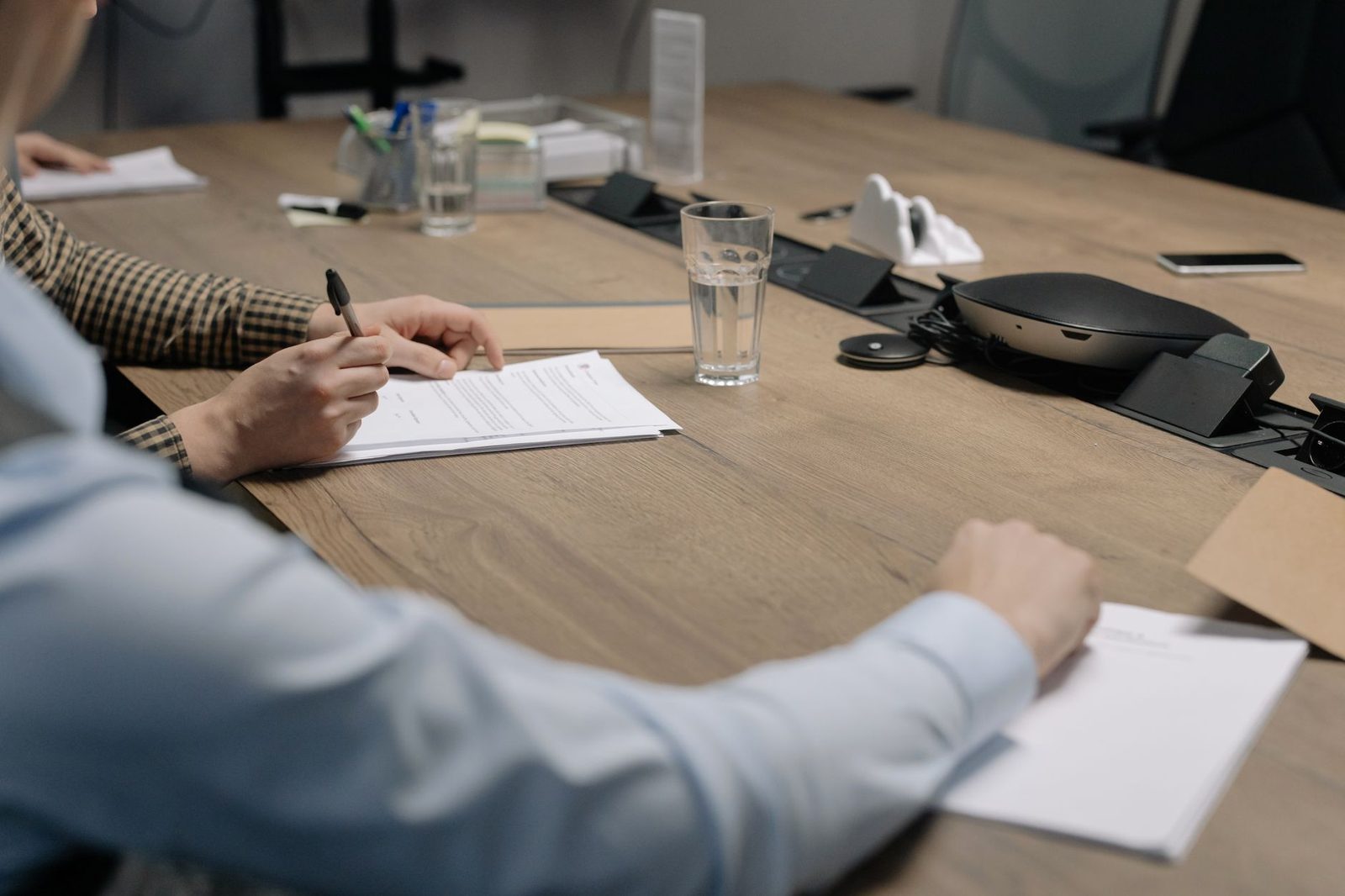 Two professionals sign documents across a conference table during a business deal closing.