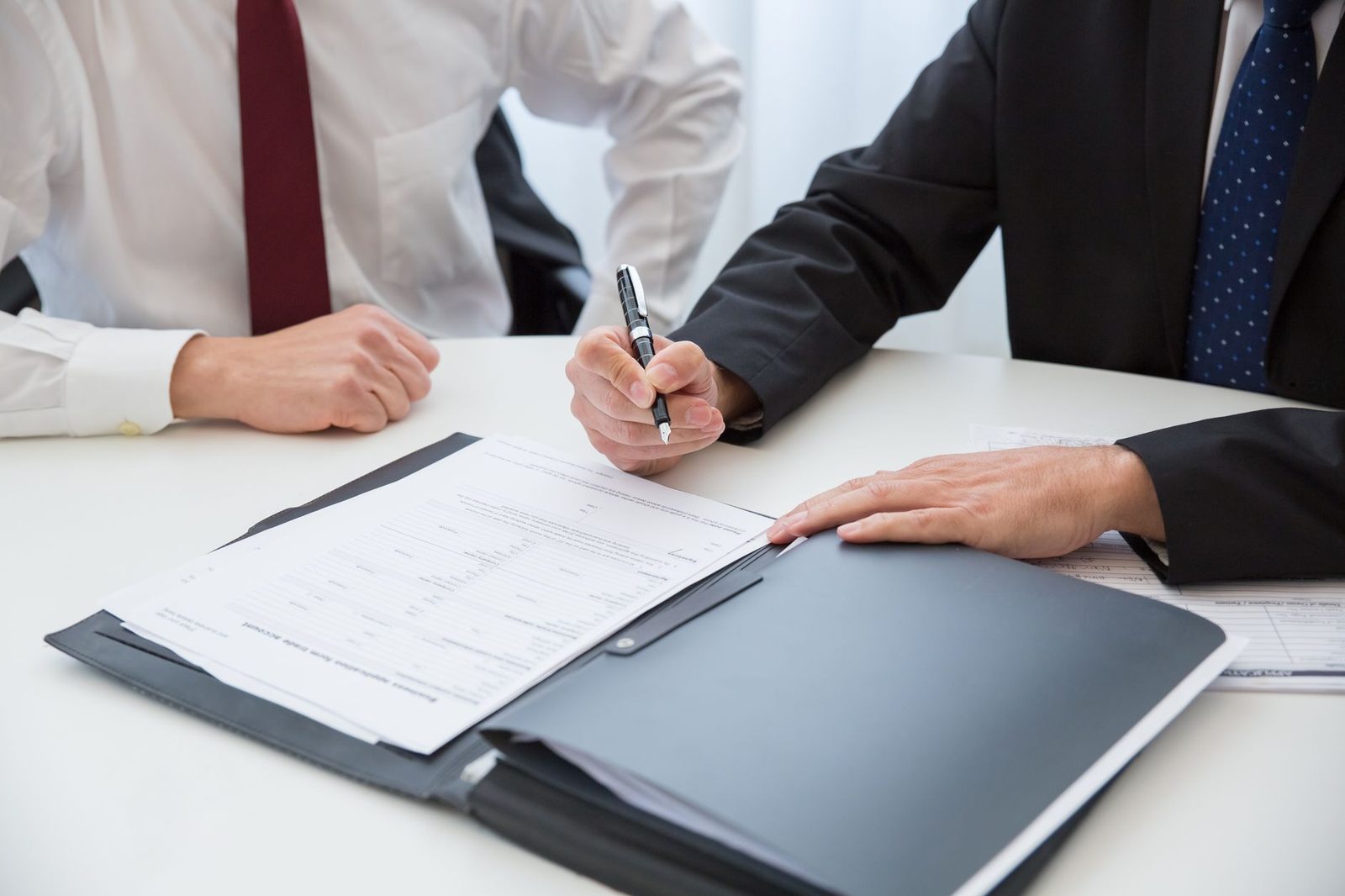 Two business professionals sign a contract across a conference table in a bright office.