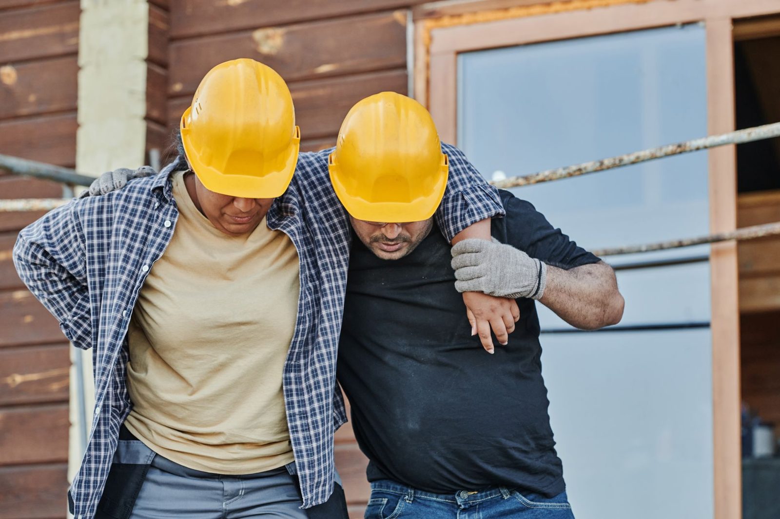 Two construction workers in hard hats help each other on a building site.