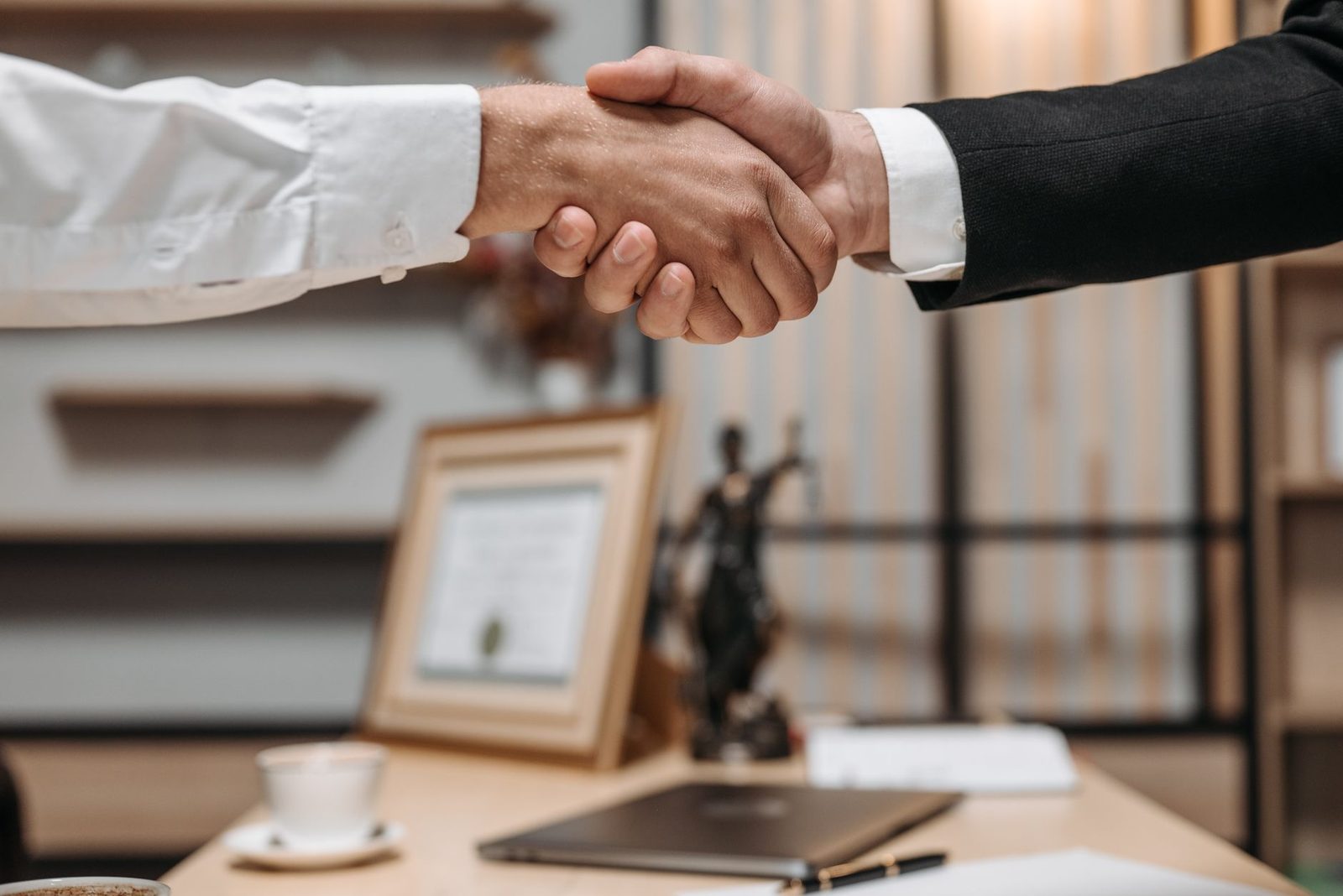 Two professionals shake hands across a desk in a modern office.