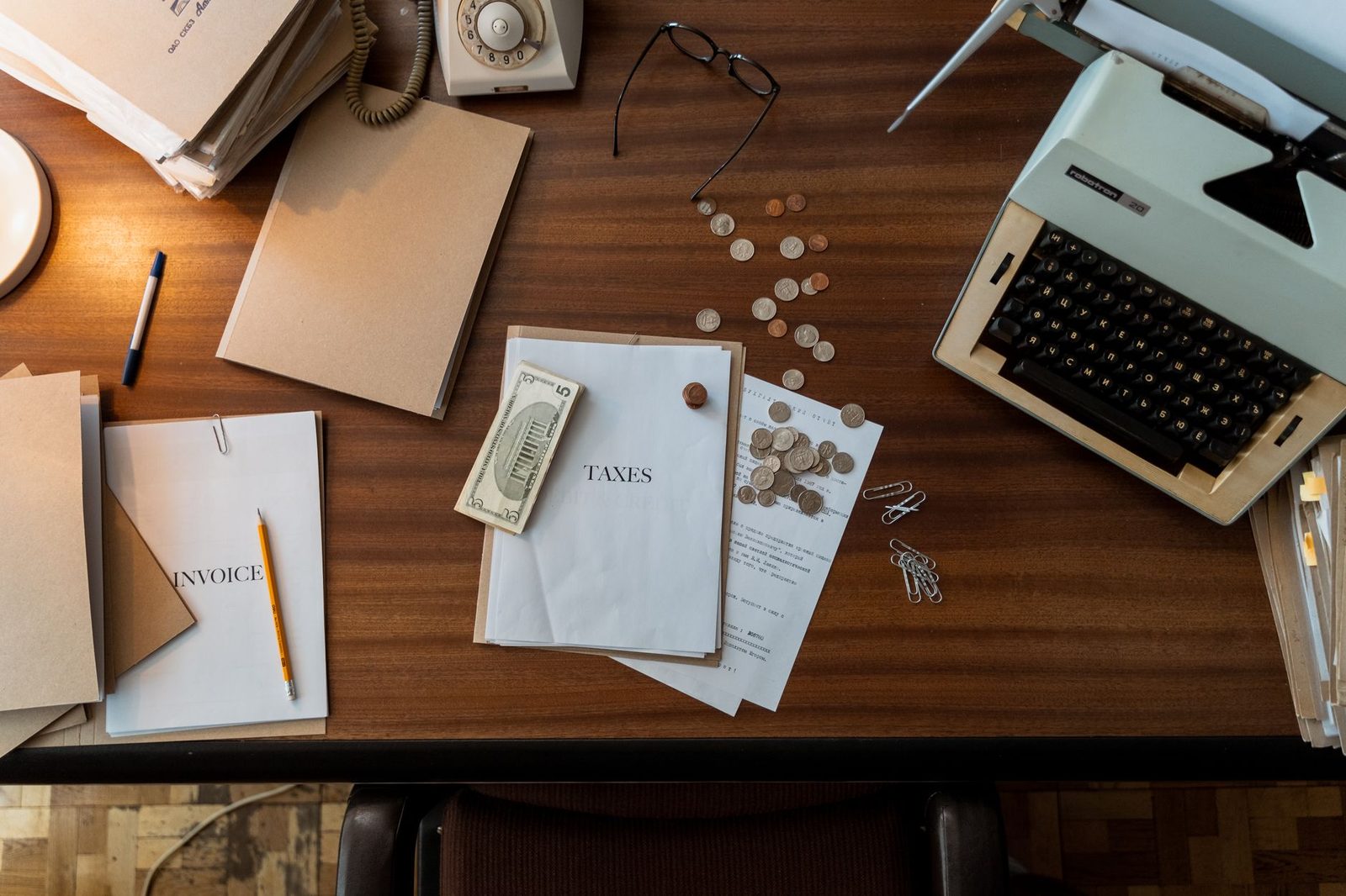 Máquina de escribir antigua con monedas sueltas y papeles sobre un escritorio de madera.