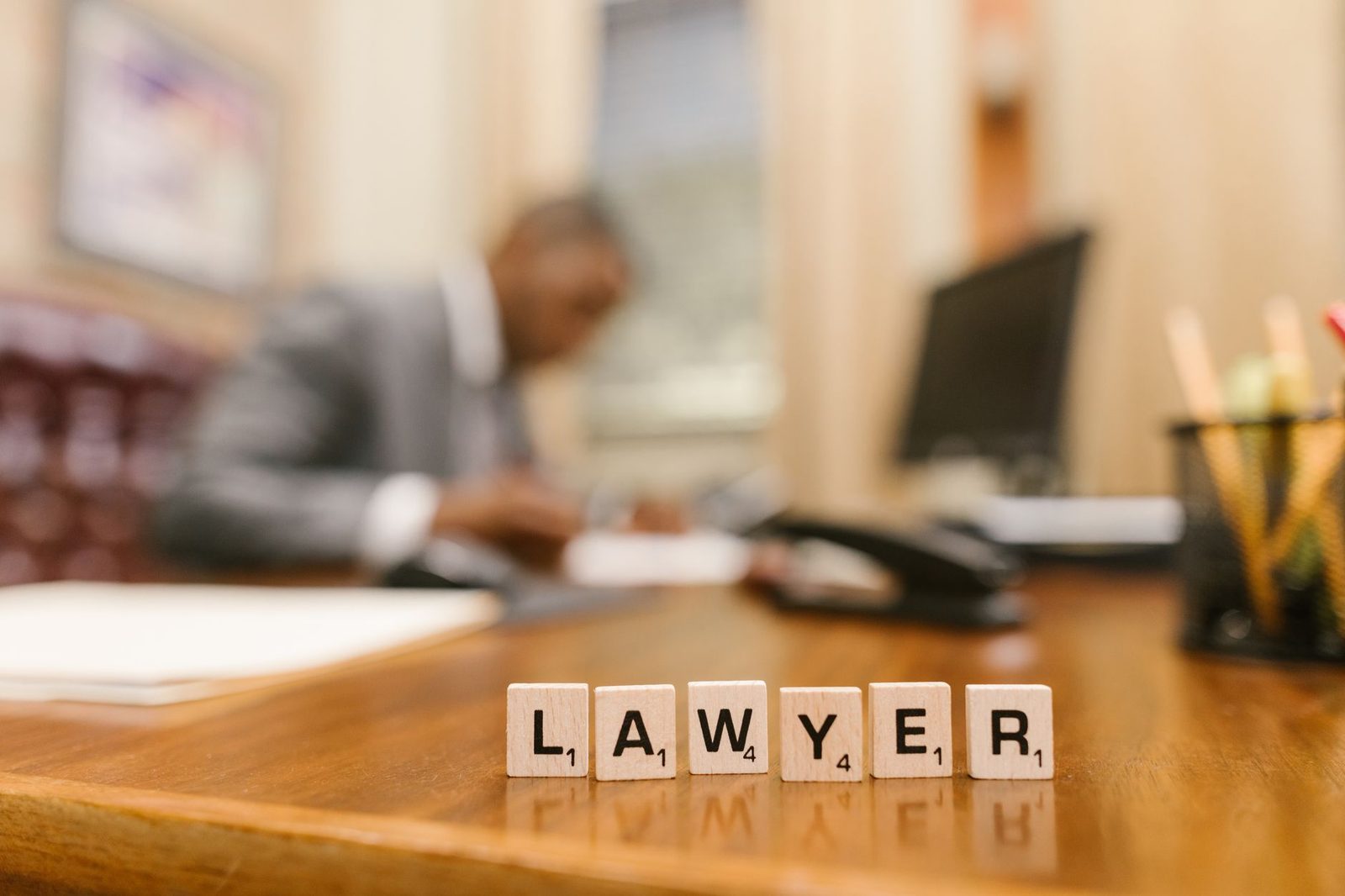 Letras de madera que deletran "LAWYER" sobre un escritorio en una oficina desenfocada.
