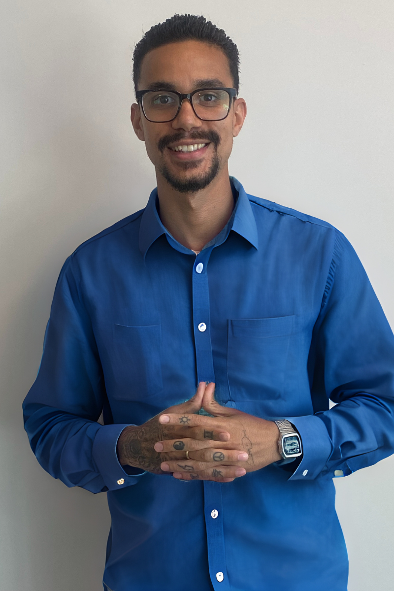 Smiling person in blue shirt with folded hands.