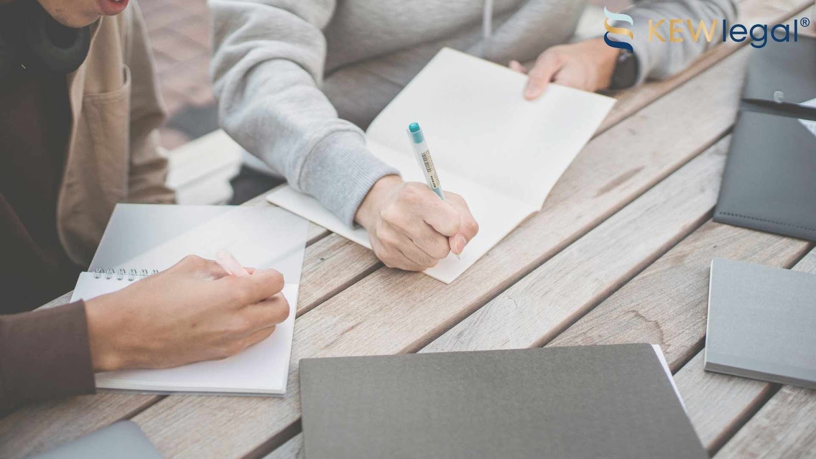 People writing notes at a wooden table.