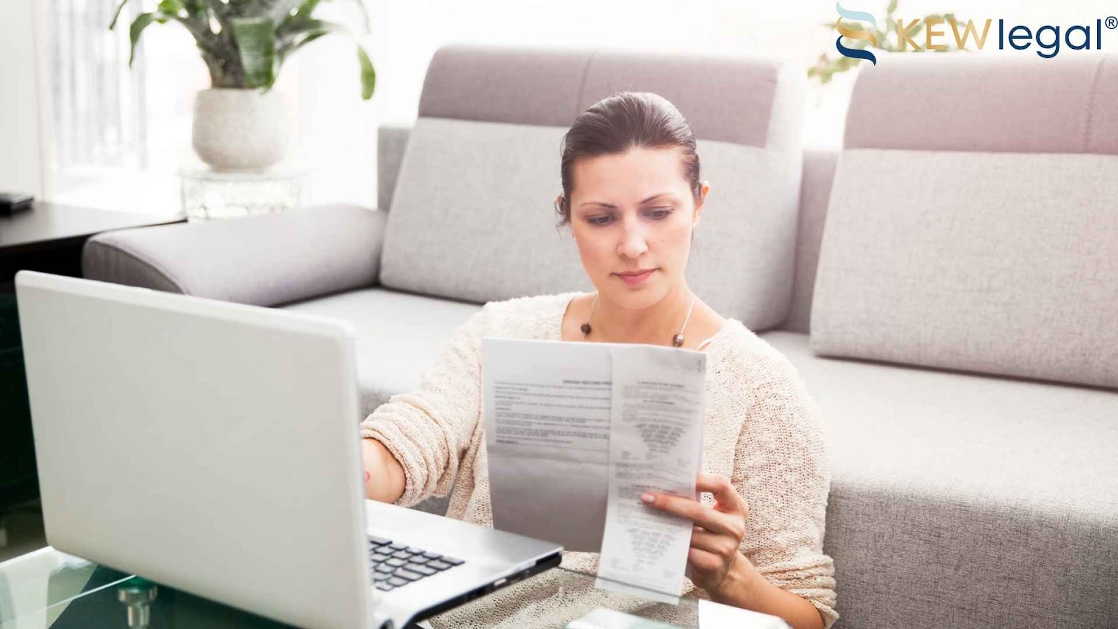 Woman reading documents near laptop on couch.