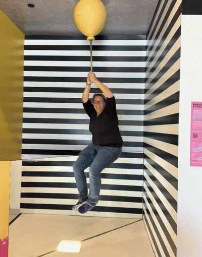 Person hanging from large yellow balloon indoors